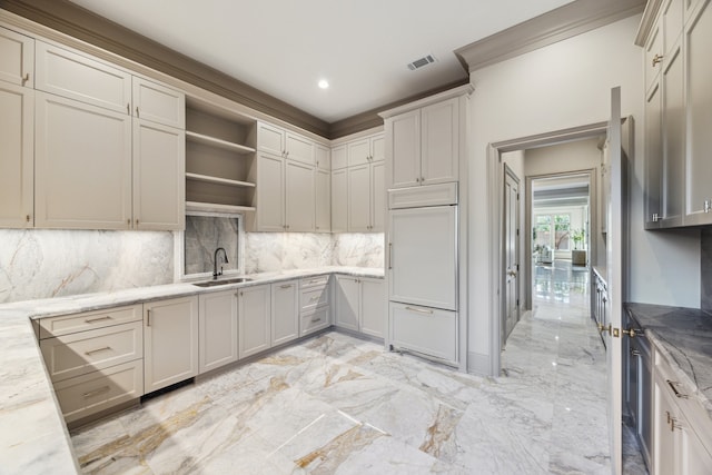 kitchen with sink, tasteful backsplash, paneled refrigerator, ornamental molding, and light stone countertops