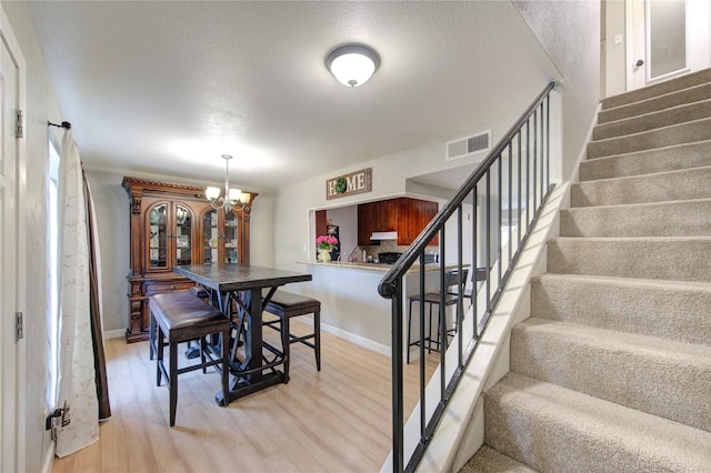 dining area featuring light wood-type flooring, an inviting chandelier, and a textured ceiling