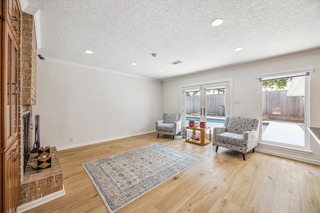 sitting room featuring ornamental molding, a stone fireplace, a textured ceiling, and light hardwood / wood-style flooring