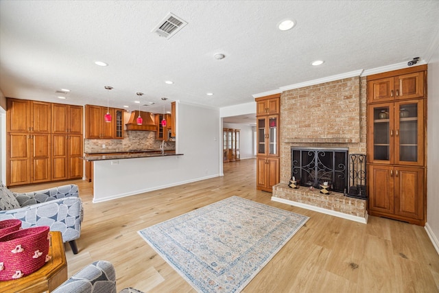 living room with light wood-type flooring, a brick fireplace, crown molding, and a textured ceiling