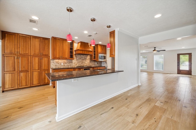 kitchen featuring pendant lighting, dark stone countertops, a kitchen breakfast bar, stainless steel microwave, and custom range hood