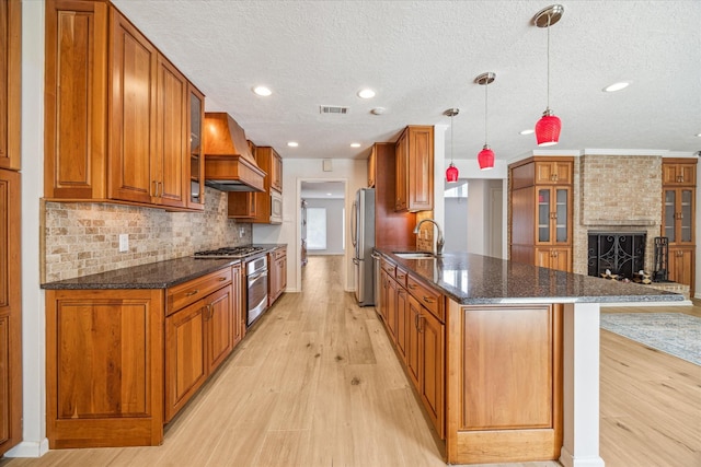 kitchen with dark stone countertops, pendant lighting, custom exhaust hood, a large fireplace, and sink