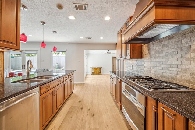 kitchen with dark stone countertops, premium range hood, pendant lighting, sink, and appliances with stainless steel finishes