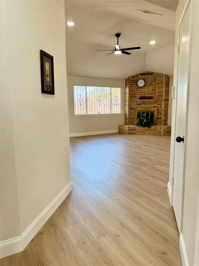 unfurnished living room featuring a brick fireplace, light hardwood / wood-style flooring, ceiling fan, and vaulted ceiling