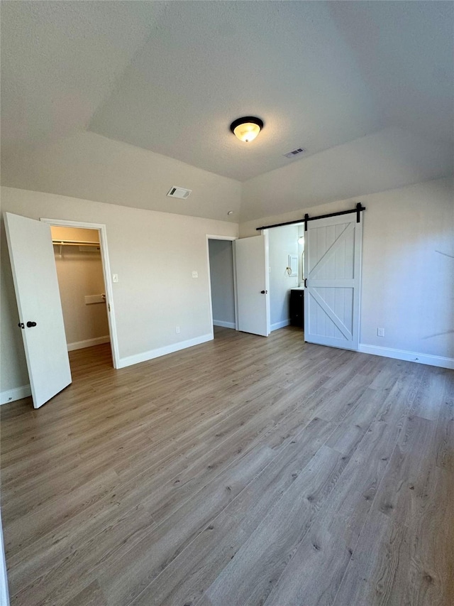 unfurnished bedroom featuring a barn door, a closet, lofted ceiling, a walk in closet, and light hardwood / wood-style flooring