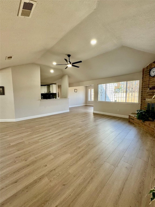 unfurnished living room with ceiling fan, light hardwood / wood-style floors, a textured ceiling, and lofted ceiling