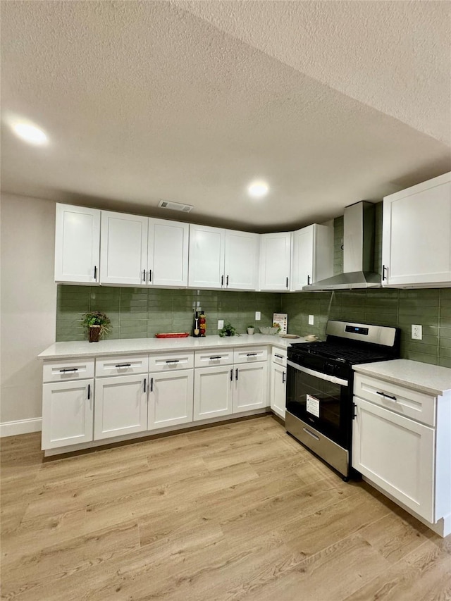 kitchen with white cabinets, stainless steel gas range, wall chimney range hood, tasteful backsplash, and light hardwood / wood-style flooring