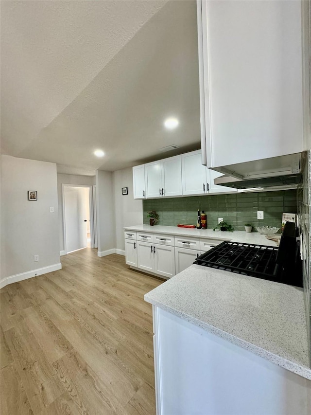 kitchen featuring light stone countertops, white cabinets, gas stove, light hardwood / wood-style floors, and backsplash