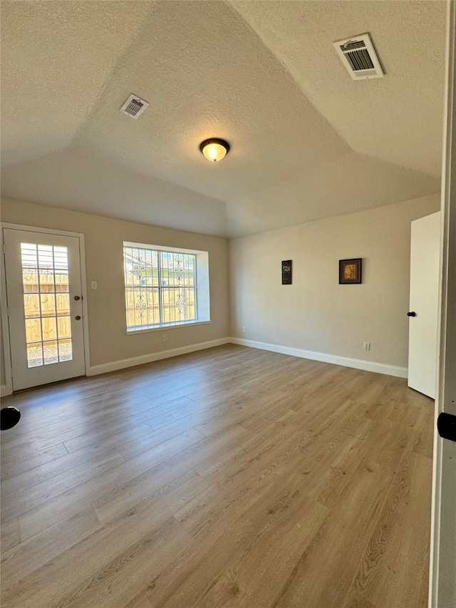 unfurnished room featuring light hardwood / wood-style floors, plenty of natural light, a textured ceiling, and lofted ceiling