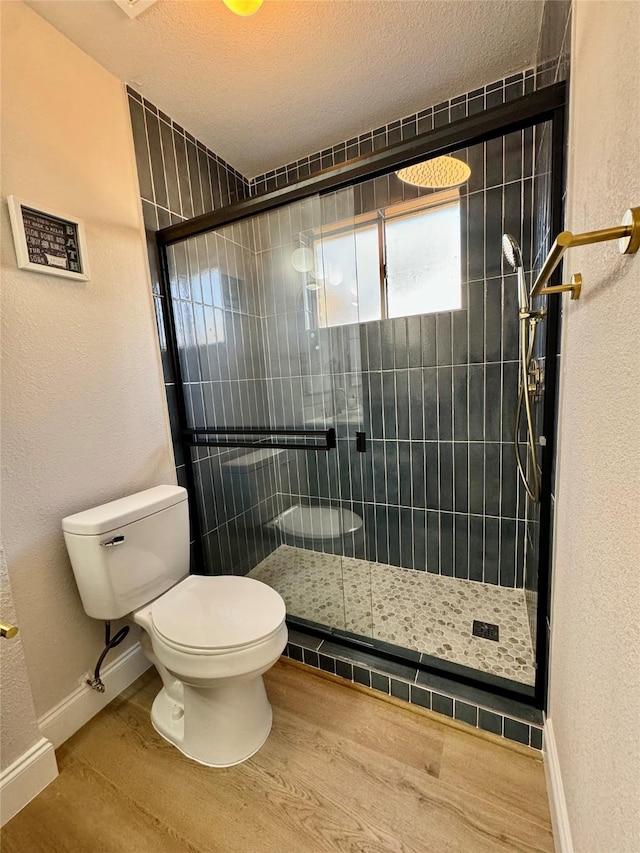 bathroom with a shower with shower door, hardwood / wood-style floors, toilet, and a textured ceiling