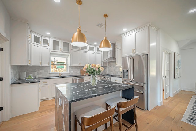 kitchen with white cabinets, appliances with stainless steel finishes, wall chimney exhaust hood, a kitchen island, and a kitchen breakfast bar