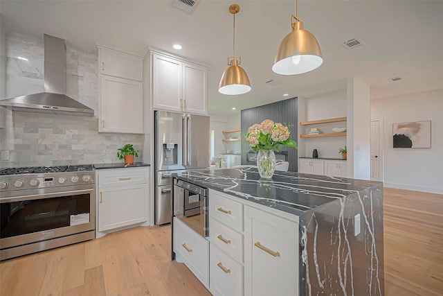 kitchen featuring appliances with stainless steel finishes, white cabinets, tasteful backsplash, and wall chimney range hood