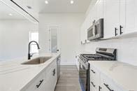 kitchen with light stone countertops, white cabinets, appliances with stainless steel finishes, and sink