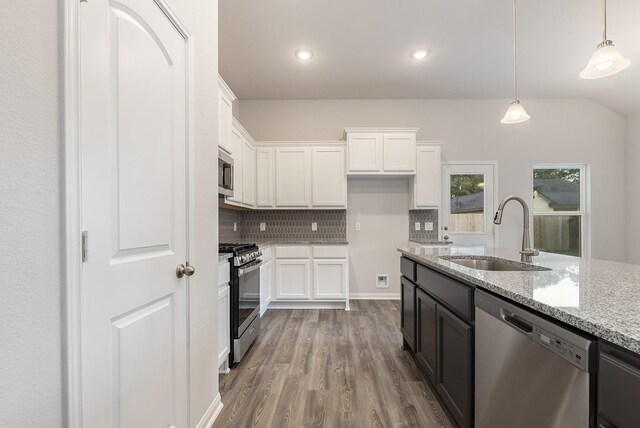 kitchen with stainless steel appliances, white cabinetry, light stone counters, and sink