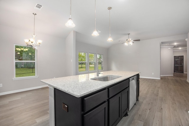 kitchen featuring an island with sink, stainless steel dishwasher, ceiling fan with notable chandelier, light stone counters, and sink