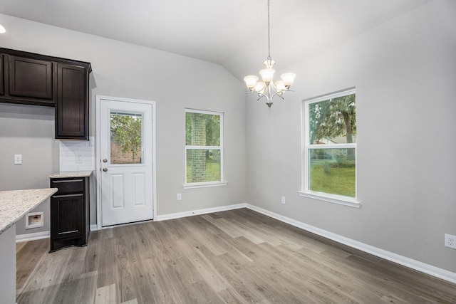 unfurnished dining area featuring vaulted ceiling, a chandelier, and light hardwood / wood-style flooring