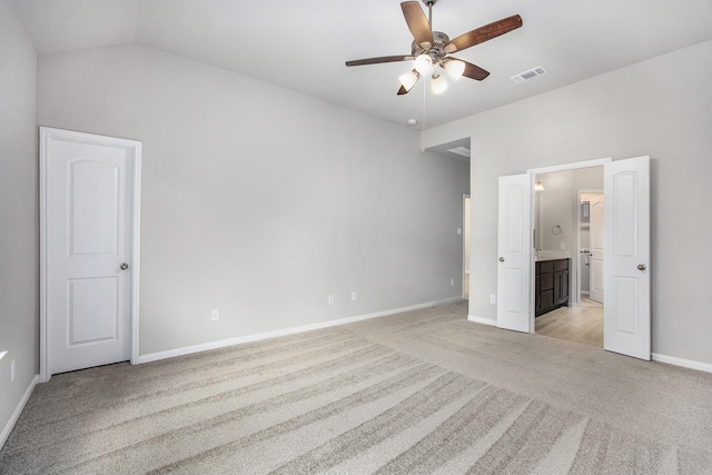 unfurnished bedroom featuring ceiling fan, light colored carpet, vaulted ceiling, and ensuite bath