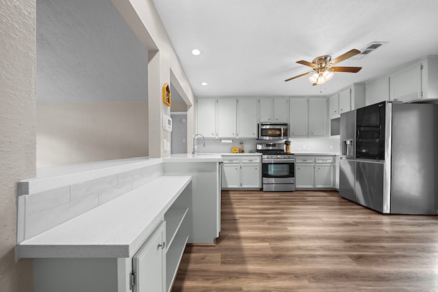 kitchen with kitchen peninsula, ceiling fan, stainless steel appliances, dark hardwood / wood-style floors, and sink