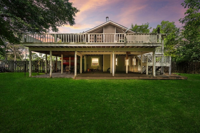 back house at dusk featuring a lawn, a deck, and a patio