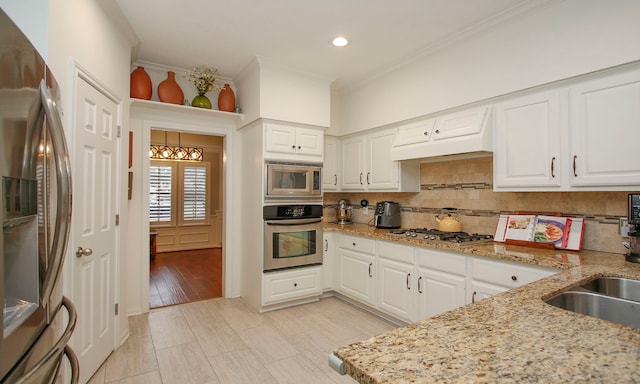 kitchen featuring tasteful backsplash, white cabinetry, appliances with stainless steel finishes, ornamental molding, and light stone counters