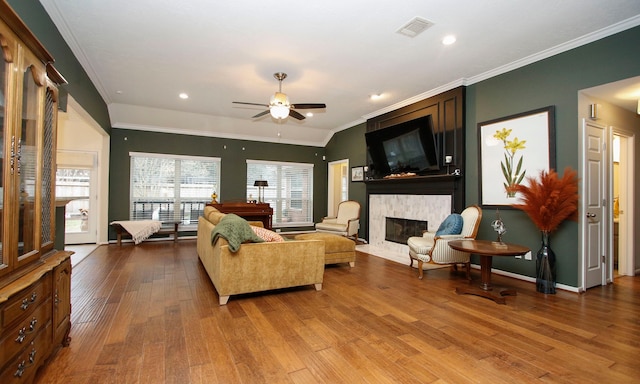 living room featuring ceiling fan, a fireplace, wood-type flooring, vaulted ceiling, and crown molding