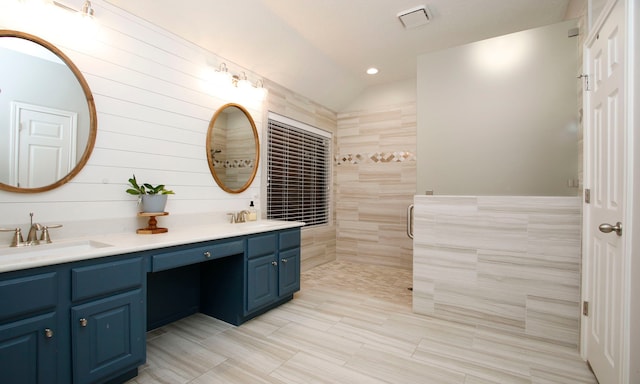 bathroom with tile walls, tiled shower, vanity, and lofted ceiling