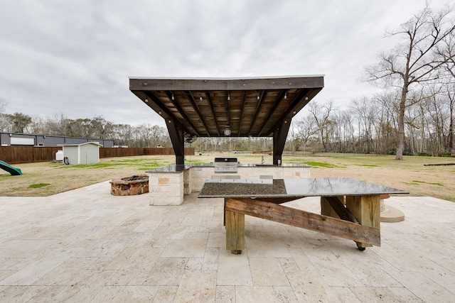 view of patio with exterior kitchen, area for grilling, an outdoor fire pit, and a storage unit