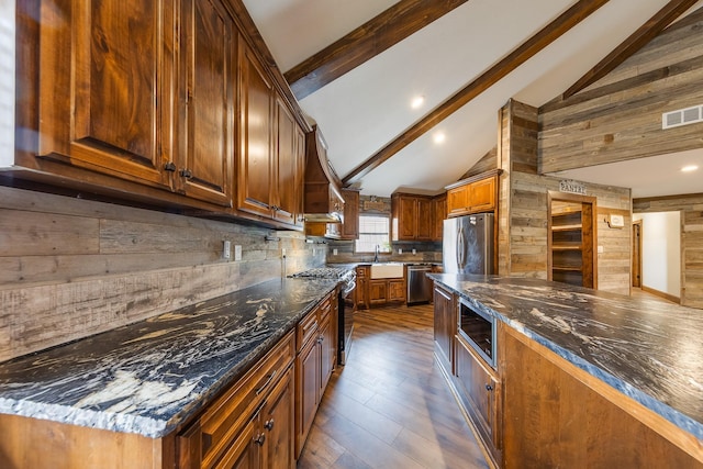 kitchen featuring beam ceiling, appliances with stainless steel finishes, dark stone countertops, and high vaulted ceiling