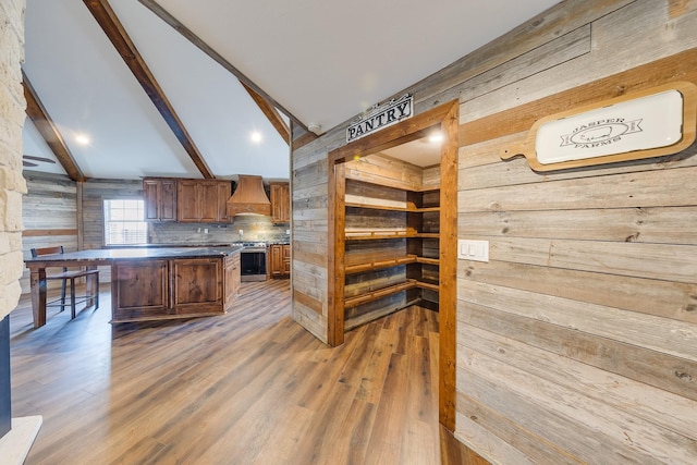 kitchen featuring premium range hood, lofted ceiling with beams, stainless steel range oven, and wood walls