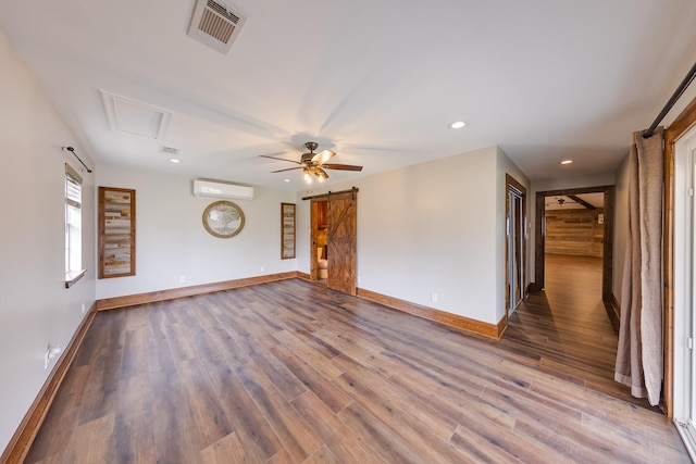 empty room featuring a wall unit AC, ceiling fan, a barn door, and hardwood / wood-style floors