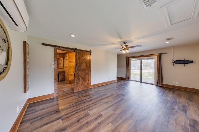 spare room featuring ceiling fan, a barn door, dark hardwood / wood-style floors, and a wall mounted air conditioner