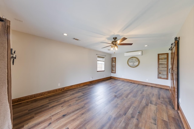 unfurnished room featuring ceiling fan, dark hardwood / wood-style flooring, a wall mounted AC, and a barn door