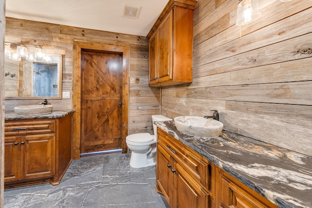 bathroom featuring toilet, wood walls, and vanity