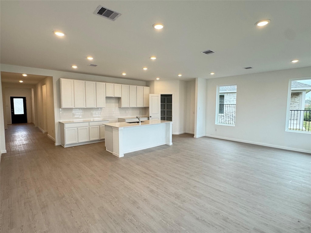 kitchen featuring sink, an island with sink, white cabinets, decorative backsplash, and light wood-type flooring