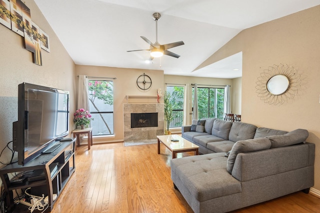 living room with lofted ceiling, a tiled fireplace, a healthy amount of sunlight, and hardwood / wood-style floors