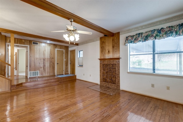 unfurnished living room with wooden walls, ceiling fan, light wood-type flooring, ornamental molding, and beam ceiling