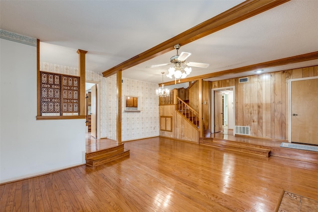 unfurnished living room featuring beam ceiling, ceiling fan, wooden walls, and light hardwood / wood-style floors