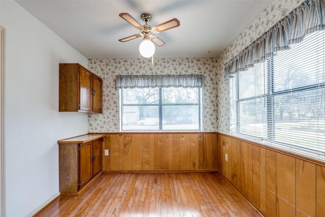 unfurnished dining area with ceiling fan, light wood-type flooring, and wood walls