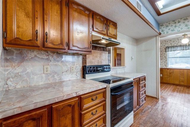 kitchen featuring a skylight, decorative backsplash, range with electric cooktop, ceiling fan, and light hardwood / wood-style flooring