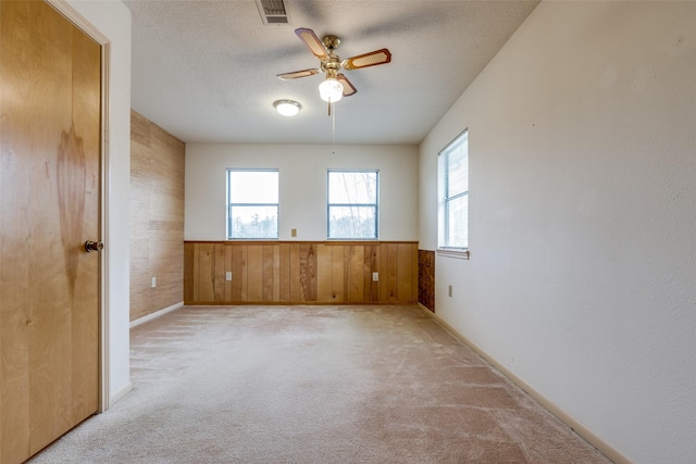 spare room with ceiling fan, light colored carpet, a textured ceiling, and wood walls