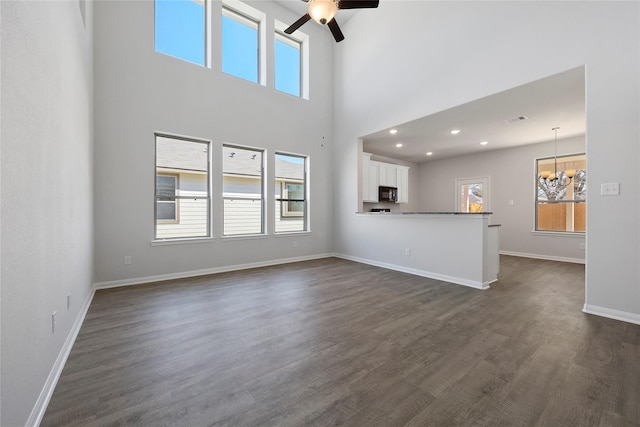 unfurnished living room with a high ceiling, a healthy amount of sunlight, dark hardwood / wood-style floors, and ceiling fan with notable chandelier