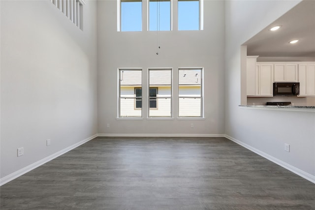 unfurnished living room featuring dark hardwood / wood-style flooring and a towering ceiling