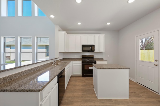 kitchen with kitchen peninsula, dark stone countertops, white cabinets, and black appliances