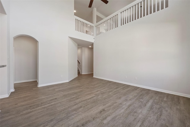 unfurnished living room with ceiling fan, a high ceiling, and hardwood / wood-style flooring