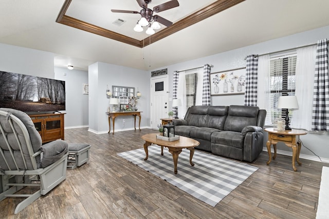 living room with ceiling fan, dark wood-type flooring, a tray ceiling, and ornamental molding