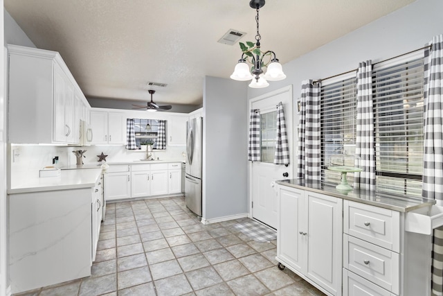 kitchen featuring ceiling fan with notable chandelier, pendant lighting, white cabinets, sink, and stainless steel refrigerator