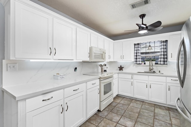 kitchen with white appliances, white cabinets, a textured ceiling, sink, and ceiling fan