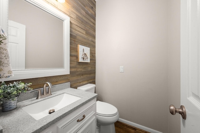 bathroom with toilet, vanity, and wood walls