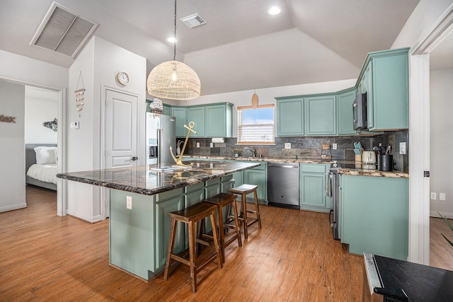 kitchen with appliances with stainless steel finishes, tasteful backsplash, vaulted ceiling, pendant lighting, and a center island