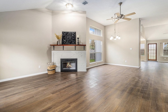 unfurnished living room with dark hardwood / wood-style flooring, a high end fireplace, lofted ceiling, and ceiling fan with notable chandelier